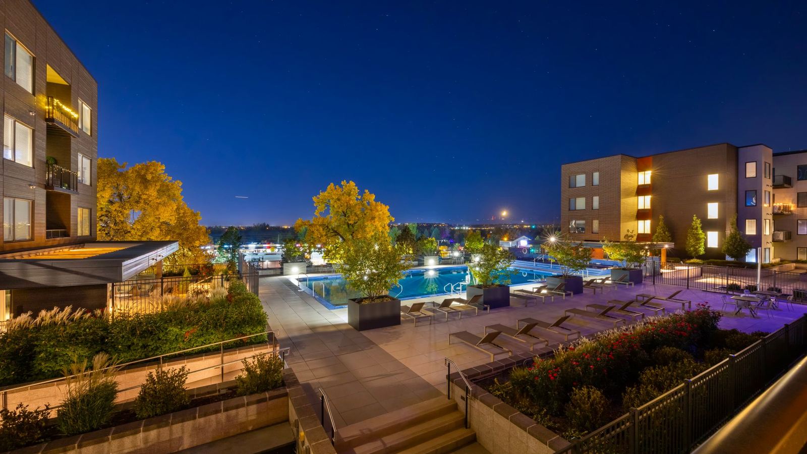 Apartment community buildings around a lit resort-style pool at dusk