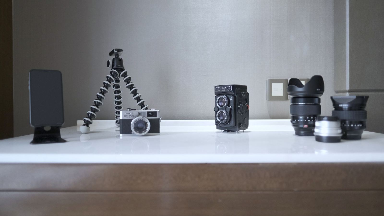 Cameras, lenses and a tripod lined up on a white shelf