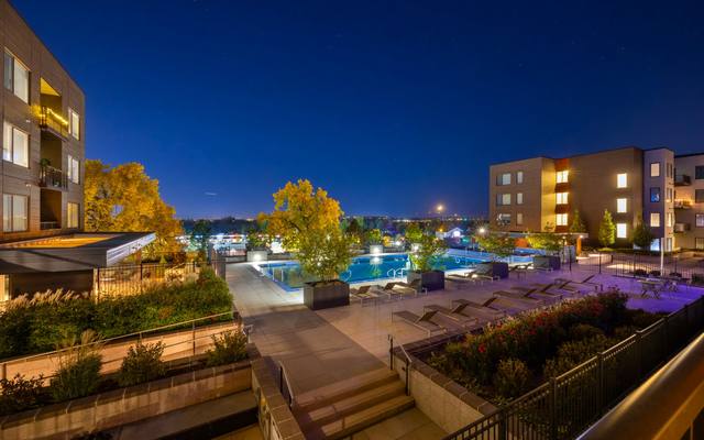 Apartment community buildings around a lit resort-style pool at dusk