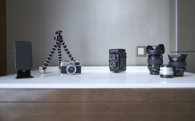 Cameras, lenses and a tripod lined up on a white shelf