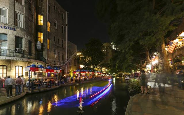 Riverside terraces and a passing barge on the San Antonio River Walk at night