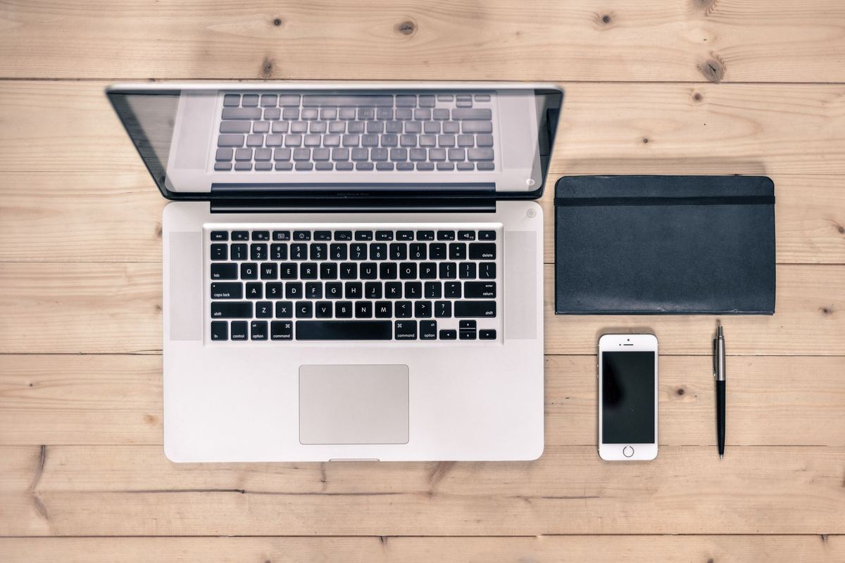 Laptop, notebook, phone and pen laid out on a wooden desk
