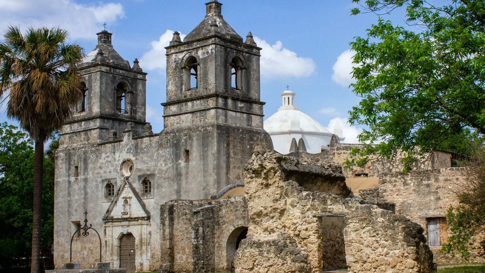 Twin bell towers of a historic San Antonio mission beside a palm tree