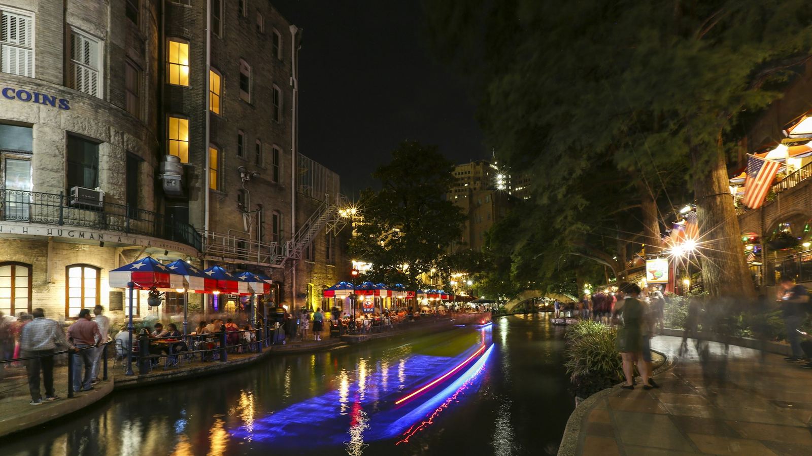 Riverside terraces and a passing barge on the San Antonio River Walk at night